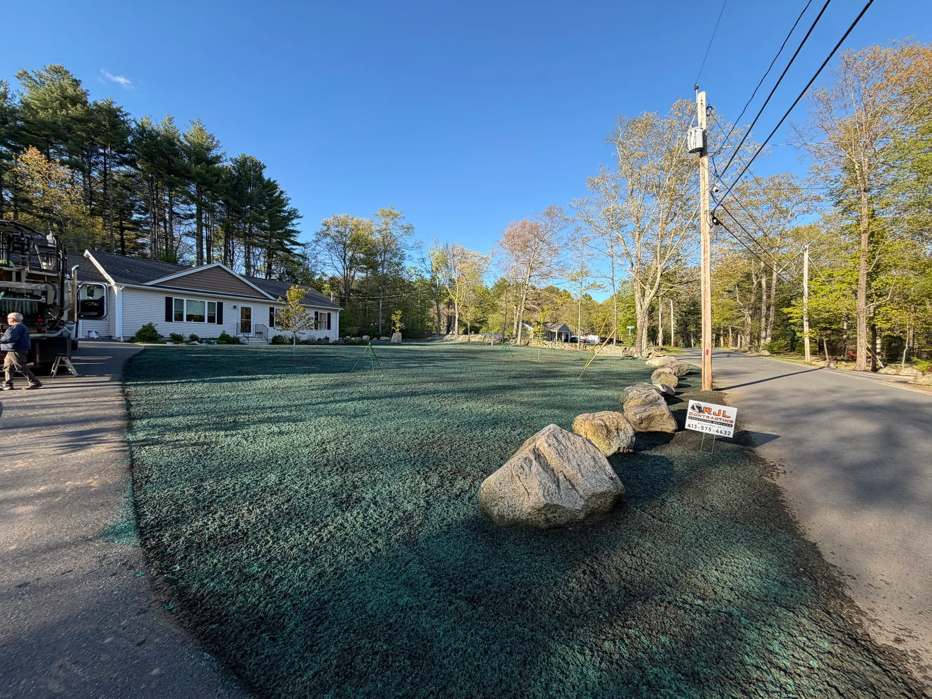 Completed hydroseeded yard restoration with granite boulder accents and RJL sign, Belchertown MA